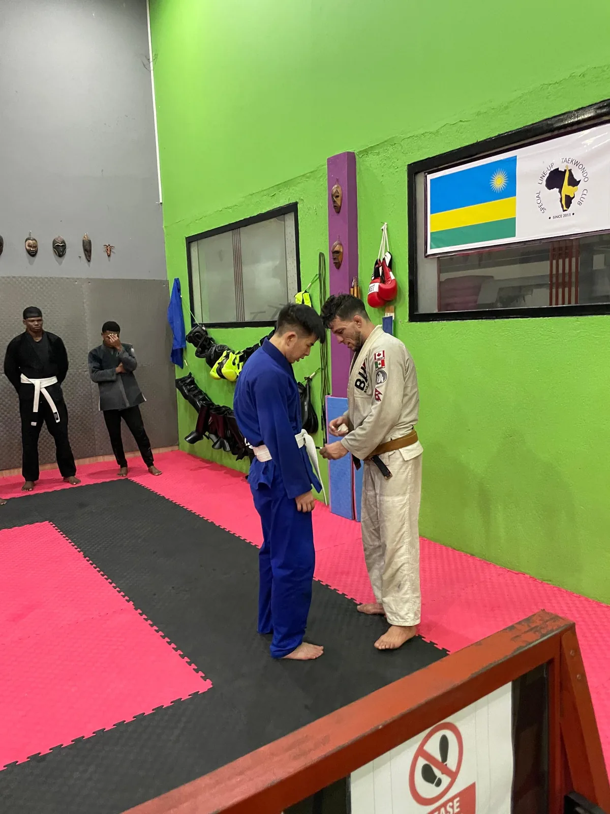A coach tying a new belt around a Kigali BJJ student